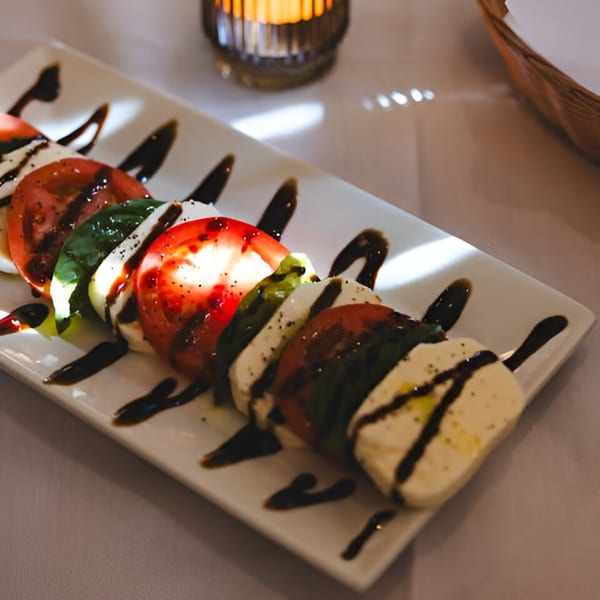 Caprese salad with sliced tomatoes, mozzarella, basil, and balsamic glaze on a white plate.