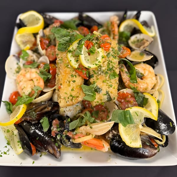 Seafood pasta with mussels, clams, shrimp, and fish, garnished with lemon and herbs.